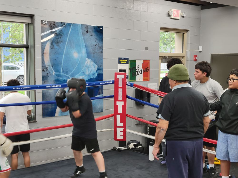 A boxer wearing headgear working mitts inside the ring, Title Boxing ropes and sparring rules sign in the background